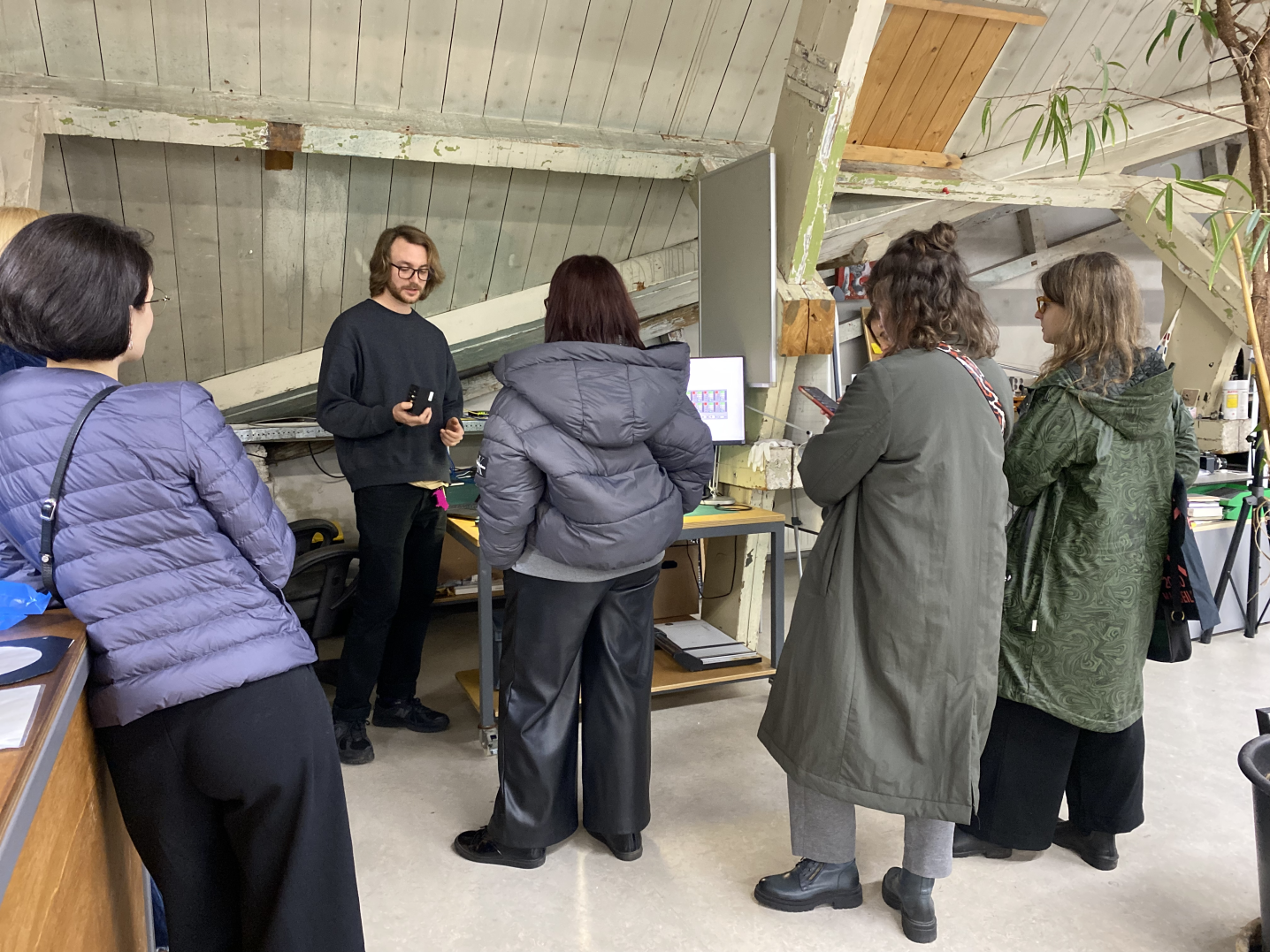 a group of people are standing in an arts workshop, listening to a man talking