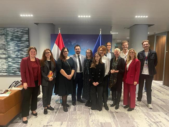 Group of people in standing next to each other in an office with flags in the background