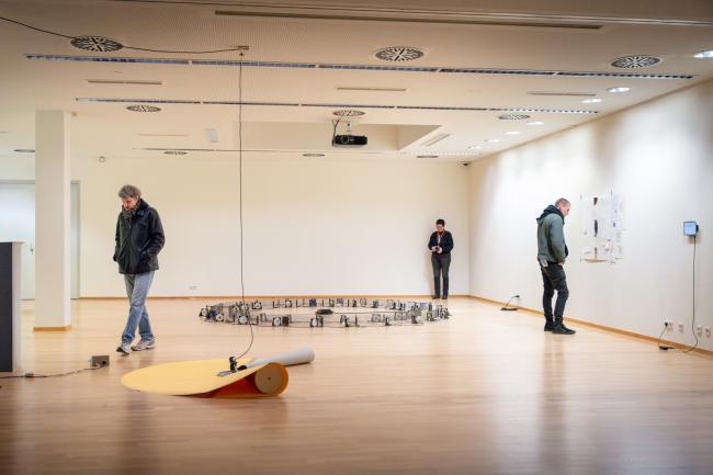 Three people looking at art installations in an exhibition room