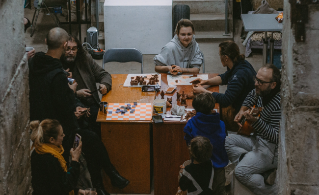 Group of people at a table chatting, playing ukelele and making clay figures