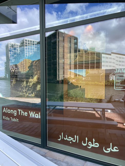 A view through a window showing photographs exhibited inside, with reflections of the buildings behind.